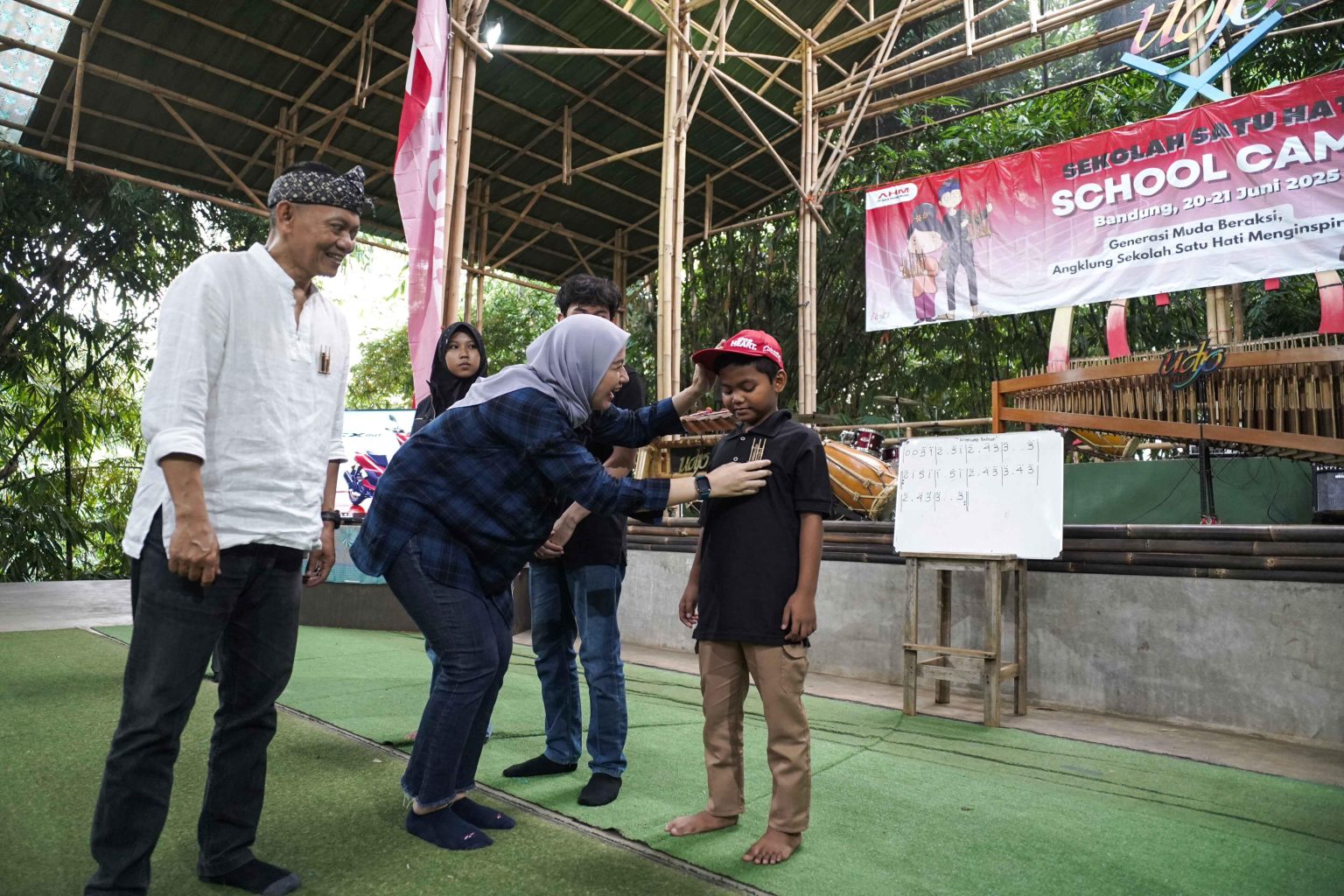 Manager Corporate Social Responsibility AHM Catur Sri Wulandari (Tengah) dan Direktur Utama PT Saung Angklung Udjo Taufik Hidayat Udjo (Kiri) melakukan penyematan pin angklung kepada peserta sebagai tanda dimulainya kegiatan School Camp 2025 (dok Honda).